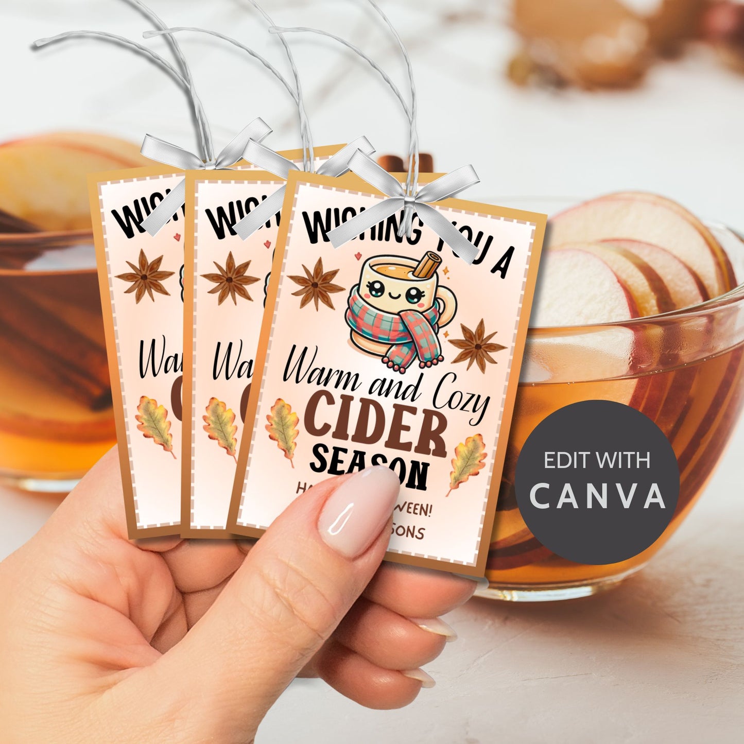 A printable Halloween gift tag featuring a warm and cozy cider theme. The tag displays a cute mug wrapped in a scarf, surrounded by autumn leaves and star anise, with the message "Wishing You a Warm and Cozy Cider Season."
