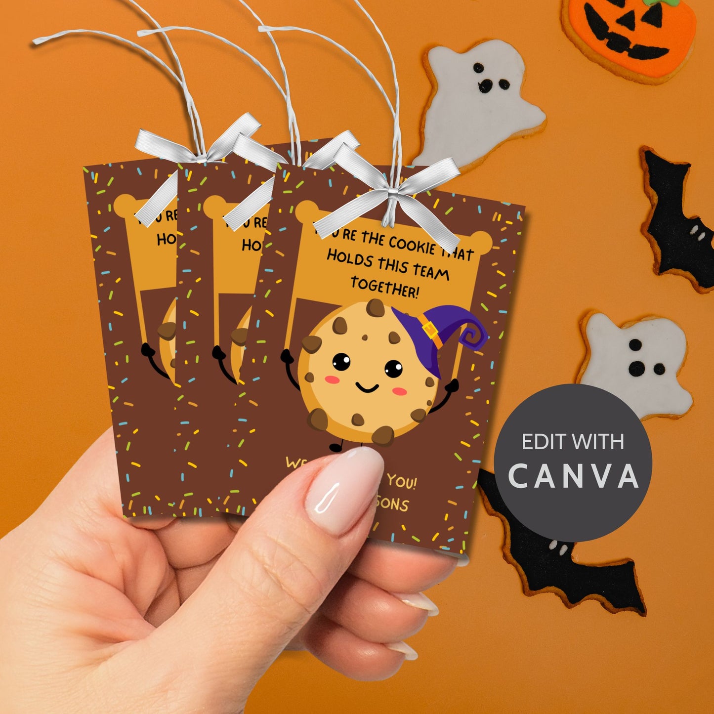 Halloween-themed printable gift tags featuring a cute cookie character in a witch's hat with a sign reading, "You're the cookie that holds this team together!" Tags are 2.5 x 3.5 inches, laid out 8 per sheet on a standard 8.5 x 11-inch page. Includes a printable PDF and a PDF with a link to an editable Canva template.
