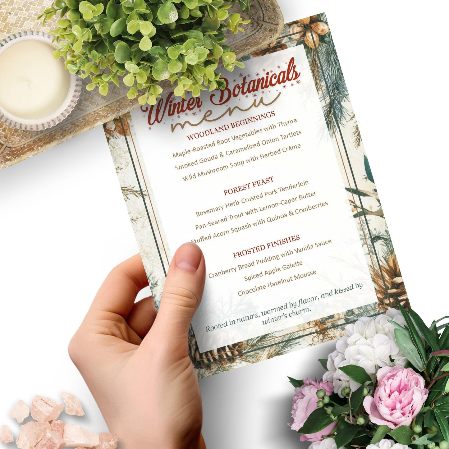 Hand holding a menu with winter botanicals theme, surrounded by flowers and a candle.