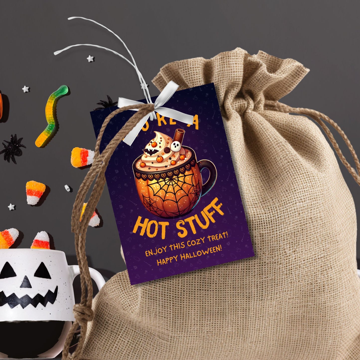 Halloween-themed printable gift tags with the message "You're a Hot Stuff" featuring a festive mug of hot cocoa on a dark purple background. Tags are 2.5 x 3.5 inches, laid out 8 per sheet on a standard 8.5 x 11-inch page. Includes a printable PDF and a PDF with a link to an editable Canva template.