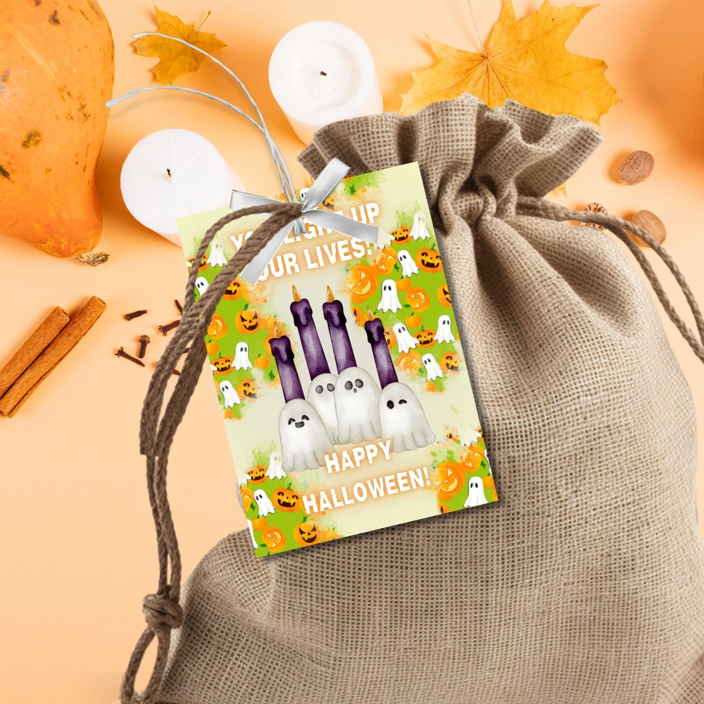 Halloween-themed printable gift tags with the message "You Light Up Our Lives!" designed for candle gifts, featuring cute ghost characters and glowing candles on a festive background. Tags are 2.5 x 3.5 inches, laid out 8 per sheet on a standard 8.5 x 11-inch page. Includes a printable PDF and a PDF with a link to an editable Canva template.