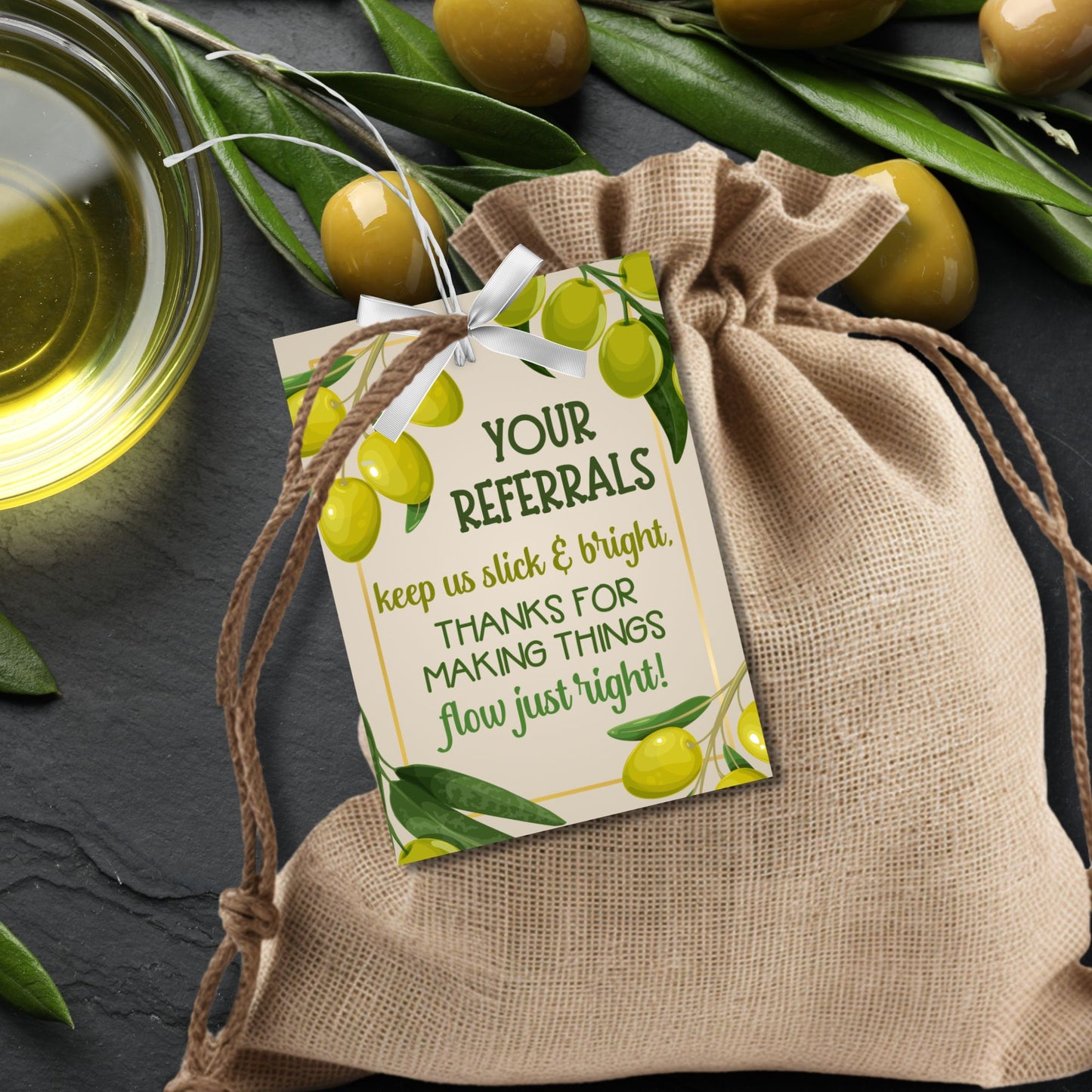 A printable PDF of olive oil-themed referral gift tags titled "Your Referrals Keep Us Slick and Bright," customizable in Canva.