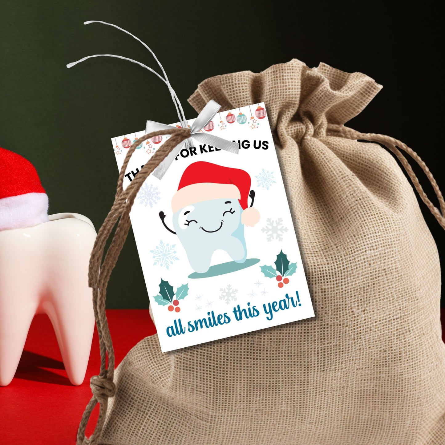 A festive set of 8 editable holiday gift tags with the message 'Thanks for Keeping Us All Smiles This Year!' featuring a smiling tooth in a Santa hat, holly, snowflakes, and hanging baubles. Perfect for dentists and dental offices to use for holiday gifts or client appreciation.