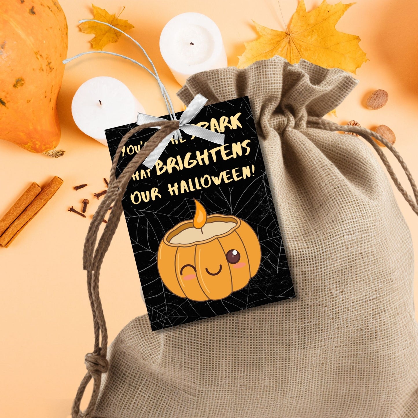 Halloween-themed printable gift tags with the message "You're the Spark that Brightens Our Halloween!" featuring a cute pumpkin candle on a black spiderweb background. Tags are 2.5 x 3.5 inches, laid out 8 per sheet on a standard 8.5 x 11-inch page. Includes a printable PDF and a PDF with a link to an editable Canva template.