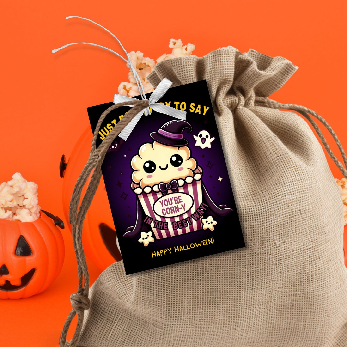 Halloween-themed printable gift tags with the message "Just Poppin' By to Say You're Corn-y in the Best Way" featuring a cute popcorn character dressed in Halloween attire. Tags are 2.5 x 3.5 inches, laid out 8 per sheet on a standard 8.5 x 11-inch page. Includes a printable PDF and a PDF with a link to an editable Canva template.