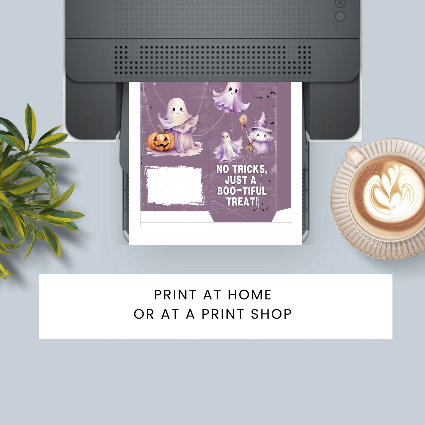 Halloween-themed card with ghosts and pumpkins being printed on a printer, with a cup of coffee and plant in the background.