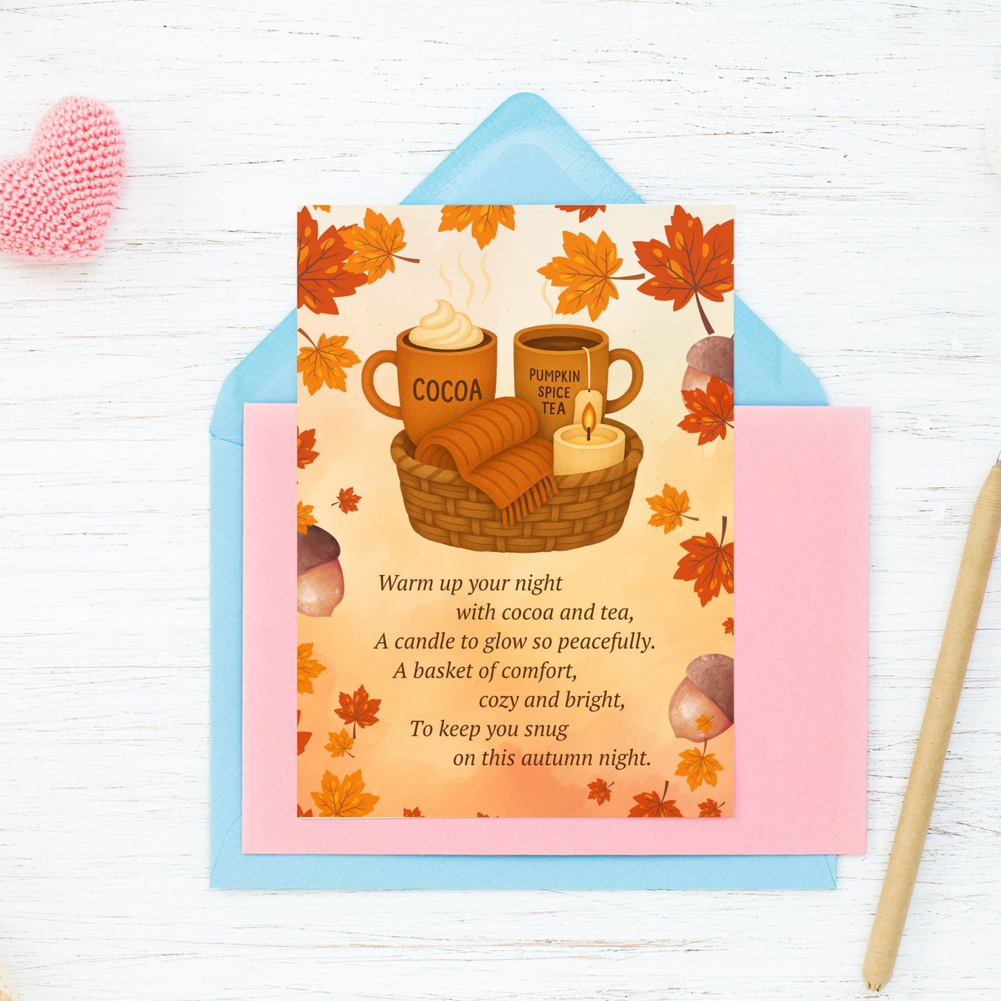 Autumn-themed card with cocoa, tea, and candle illustration on a white wooden surface.