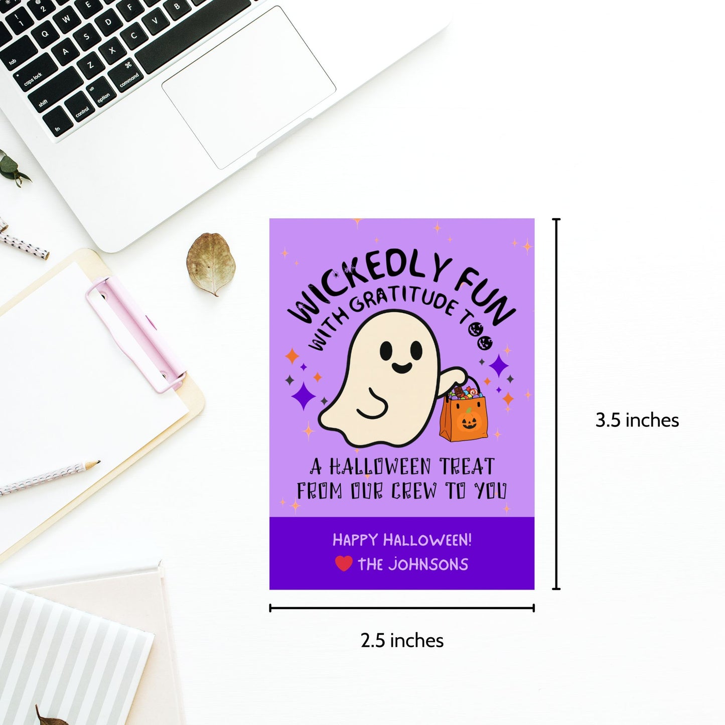 Halloween-themed card with ghost and candy bag design, placed on a desk with laptop and stationery items.