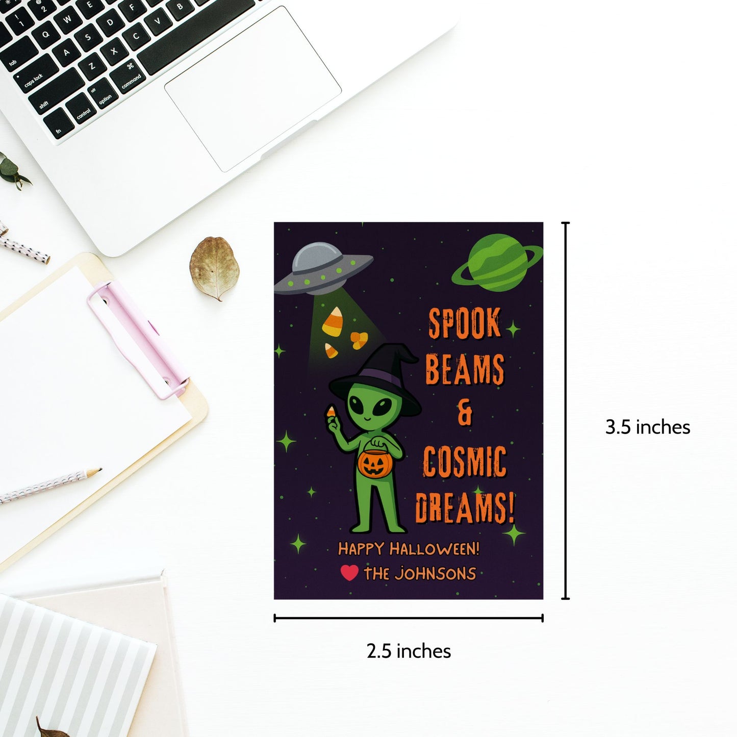 Halloween-themed card with alien design and text, placed on a desk with a laptop.