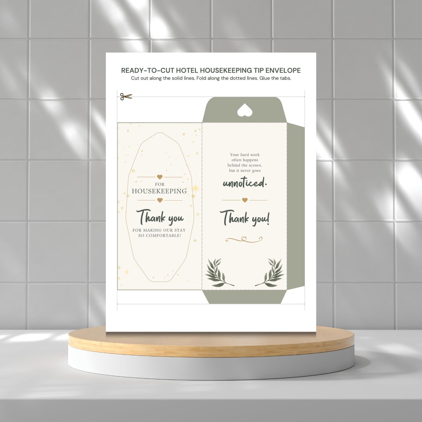 A printed housekeeping tip envelope template displayed upright on a round pedestal against a light gray tiled wall. The card shows the front and back designs with elegant typography, small gold decorative accents, and botanical line art.