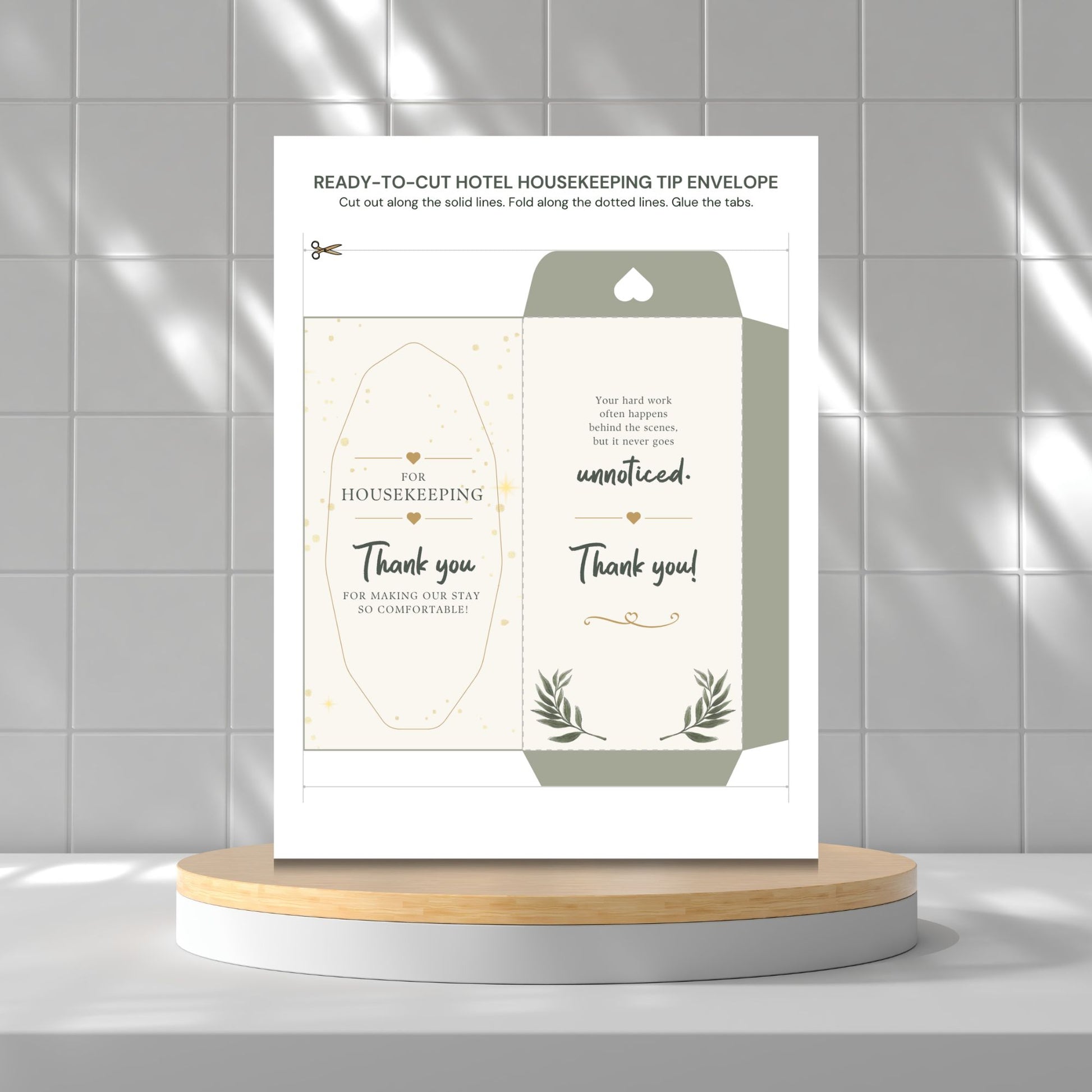A printed housekeeping tip envelope template displayed upright on a round pedestal against a light gray tiled wall. The card shows the front and back designs with elegant typography, small gold decorative accents, and botanical line art.