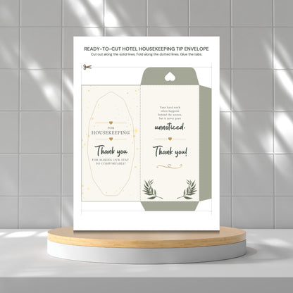 A printed housekeeping tip envelope template displayed upright on a round pedestal against a light gray tiled wall. The card shows the front and back designs with elegant typography, small gold decorative accents, and botanical line art.