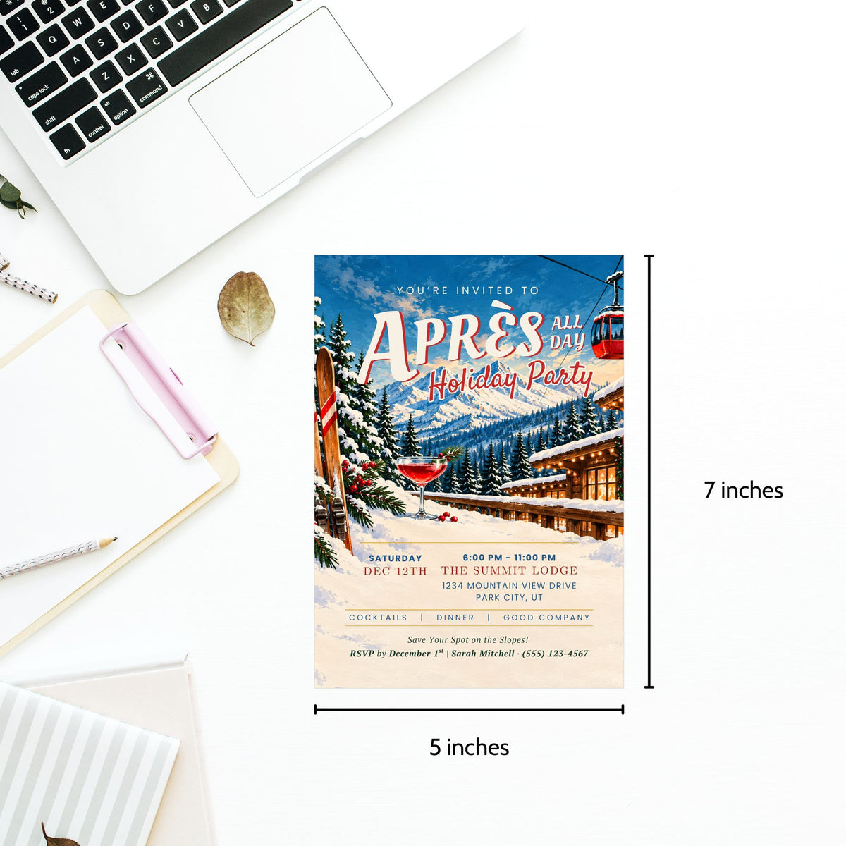 A 5x7 inch holiday party invitation card displayed on a white desk with a laptop, notebook, and pen. The invitation features a winter mountain lodge scene with red cabins, snowy trees, and a blue sky with a red gondola, and includes dimension markers showing 7 inches tall by 5 inches wide.