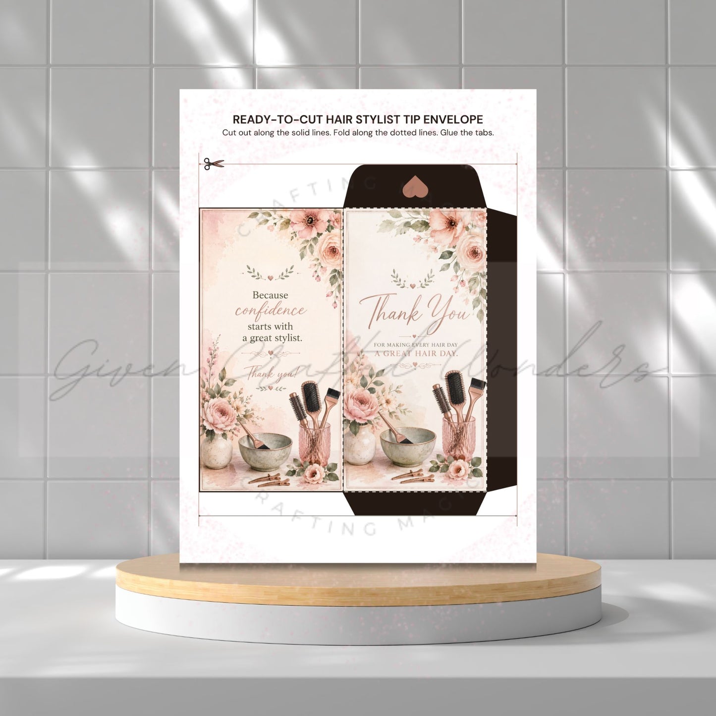 A printed hair stylist tip envelope template displayed upright on a round pedestal, with a matching folded envelope shown behind it. The design features floral illustrations, salon tools, and thank-you text, set against a light gray tiled background with soft shadow overlays.
