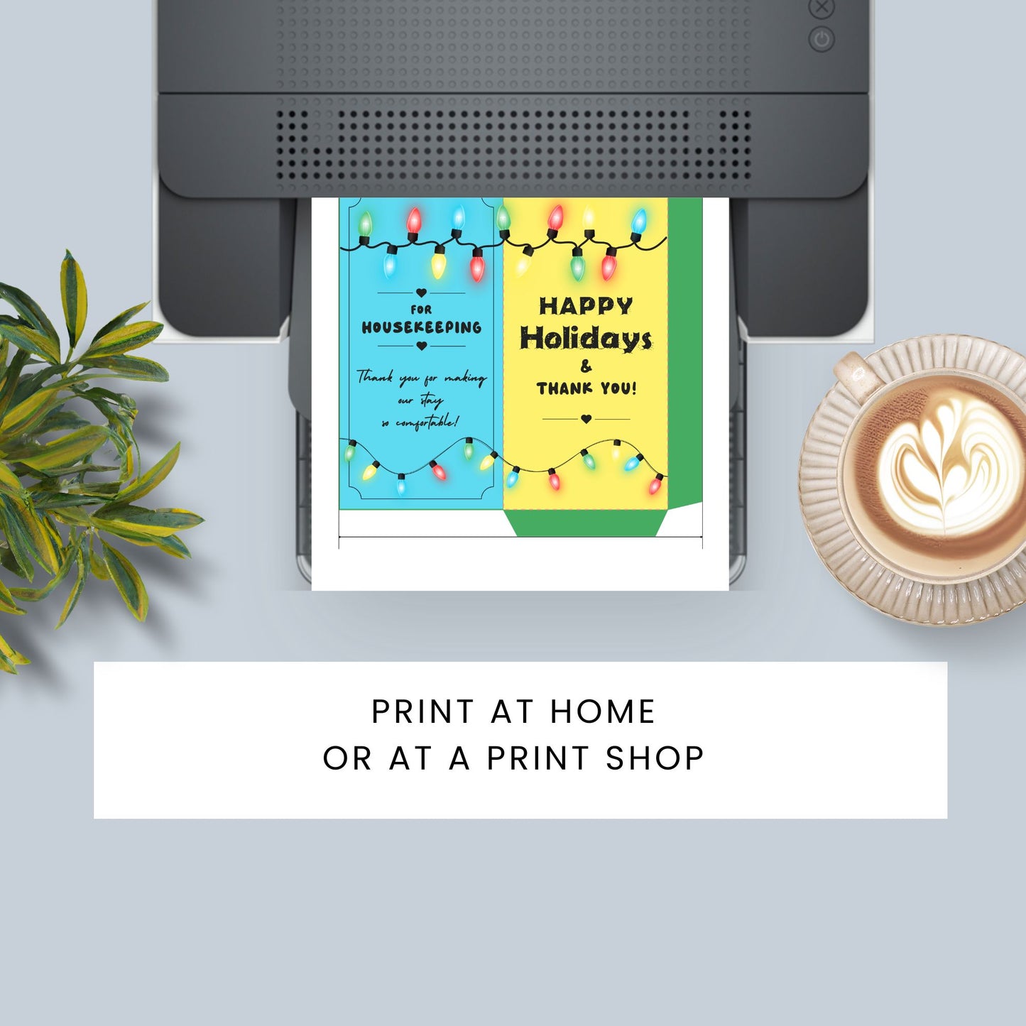 A flat-lay mockup showing a printed holiday thank-you card emerging from a black printer, with decorative text on the card reading 'HAPPY Holidays & THANK YOU!'. The scene includes a plant on the left, a cup of latte on the right, and a white banner at the bottom that says 'PRINT AT HOME OR AT A PRINT SHOP'.