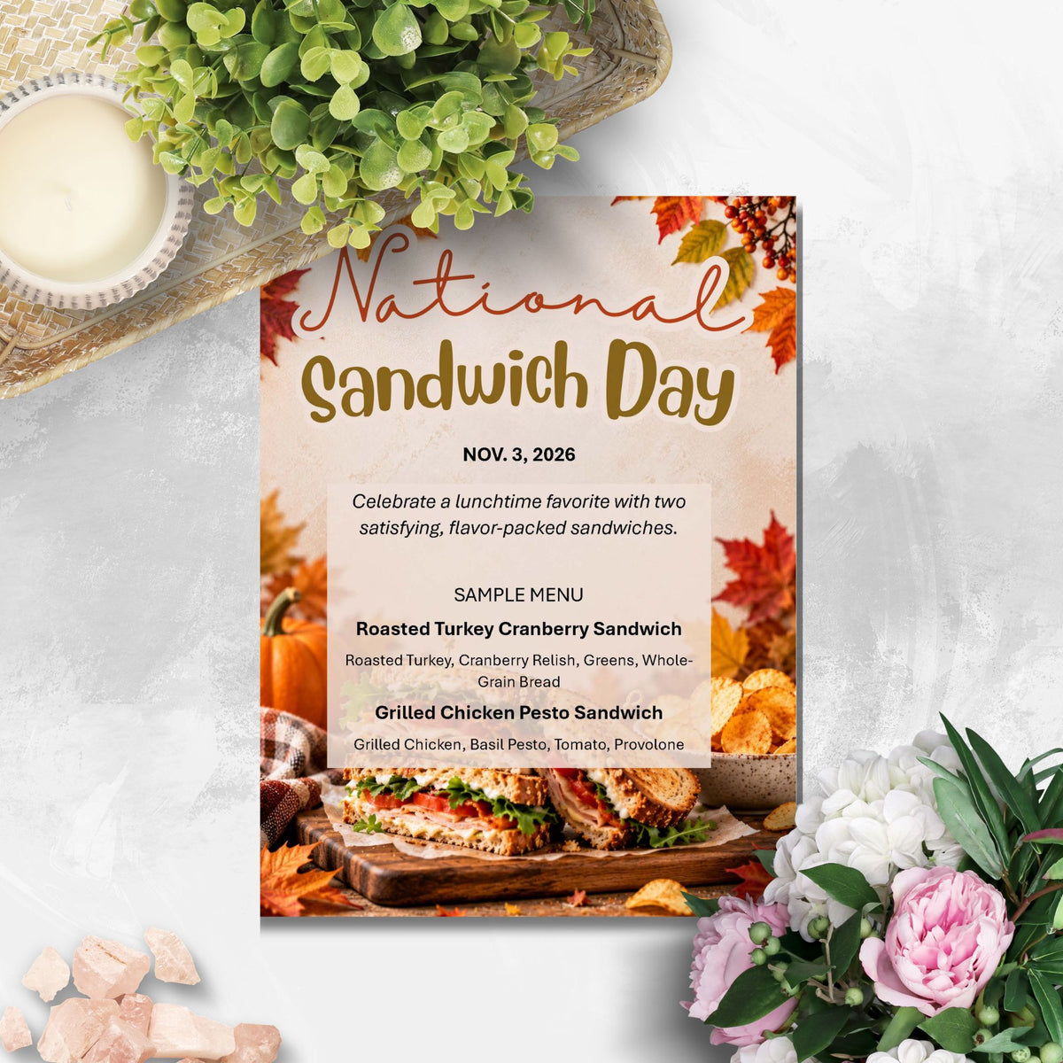 A National Sandwich Day menu card styled in a flat-lay setting with autumn leaves, flowers, and a small bowl of cream on a light marble surface. The card features a sample menu for Nov.