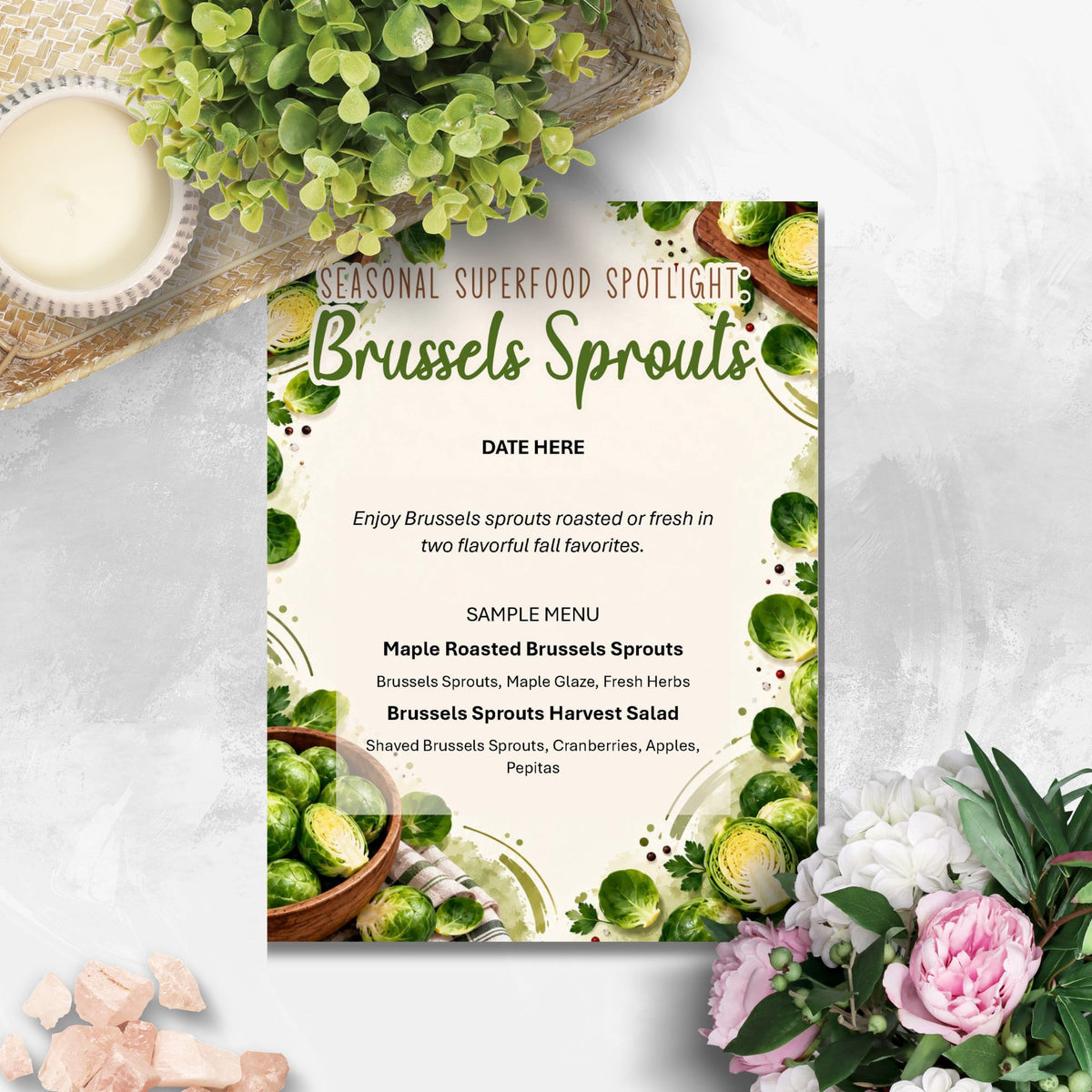 A printed menu card titled 'Seasonal Superfood Spotlight Brussels Sprouts' styled on a light stone surface with greenery, flowers, and food props around it.