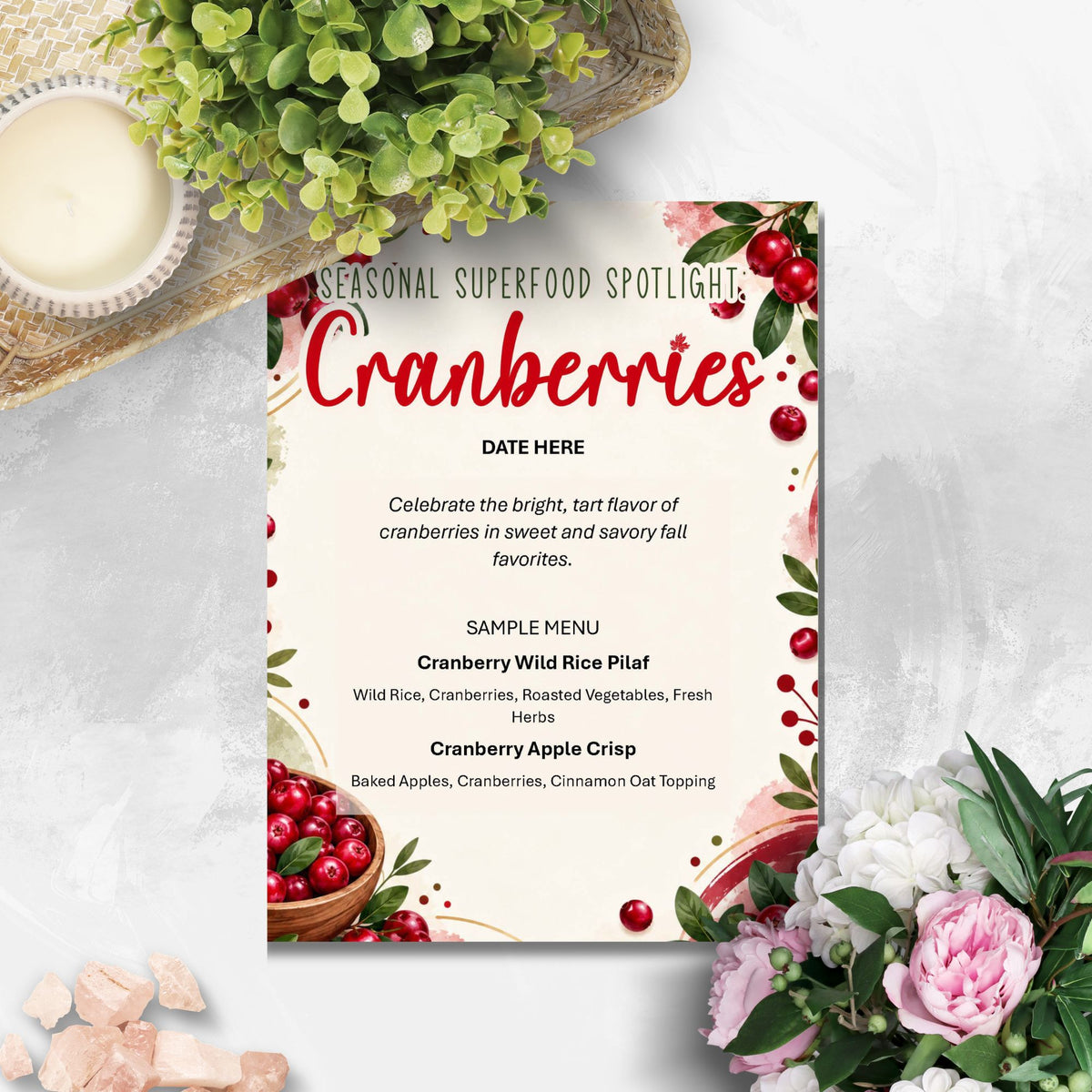 A decorative printed menu card titled 'Seasonal Superfood Spotlight: Cranberries' with red berries, green leaves, and floral accents, styled on a light surface with flowers, a bowl, and a woven mat around it.