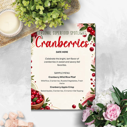 A decorative printed menu card titled 'Seasonal Superfood Spotlight: Cranberries' with red berries, green leaves, and floral accents, styled on a light surface with flowers, a bowl, and a woven mat around it.