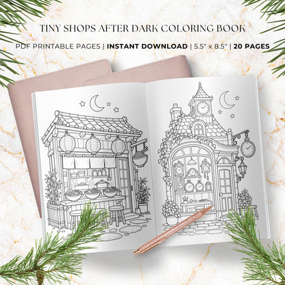 A styled flat-lay of a coloring book preview titled 'Tiny Shops After Dark Coloring Book' with two open black-and-white illustrated shop pages, a pink notebook beneath, a rose-gold pen, and pine branches on a light marble background. Text reads 'PDF Printable Pages | Instant Download | 5.