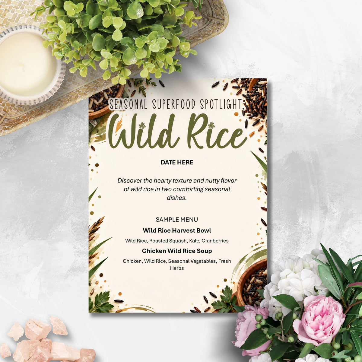 A printed menu card titled 'Seasonal Superfood Spotlight: Wild Rice' styled on a light stone surface with greenery, a candle, and pink flowers around it.