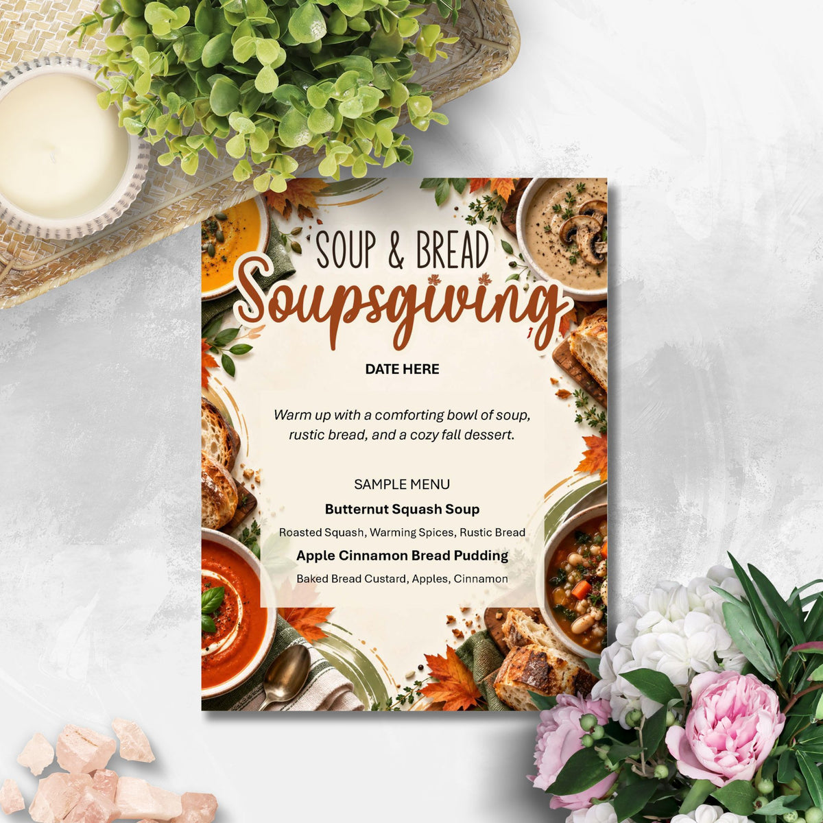 A square promotional sign for a 'Soup & Bread Soupsgiving' event is displayed on a light gray textured surface, surrounded by decorative props including a small green plant, a bowl of white sauce, and pink and white flowers. The sign features a warm autumnal food-themed border with soup and bread illustrations, and placeholder text for a sample menu.