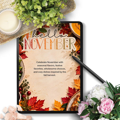 A tablet displaying a 'Hello November' autumn-themed digital planner or printable cover, styled in a flat-lay with a black stylus, flowers, a candle, and greenery on a white background.