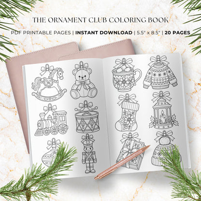 An open printable coloring book showing black-and-white holiday-themed line art pages, styled on a light marble surface with pine branches and a rose-gold pencil. Text at the top reads 'The Ornament Club Coloring Book' and 'PDF Printable Pages | Instant Download | 5.