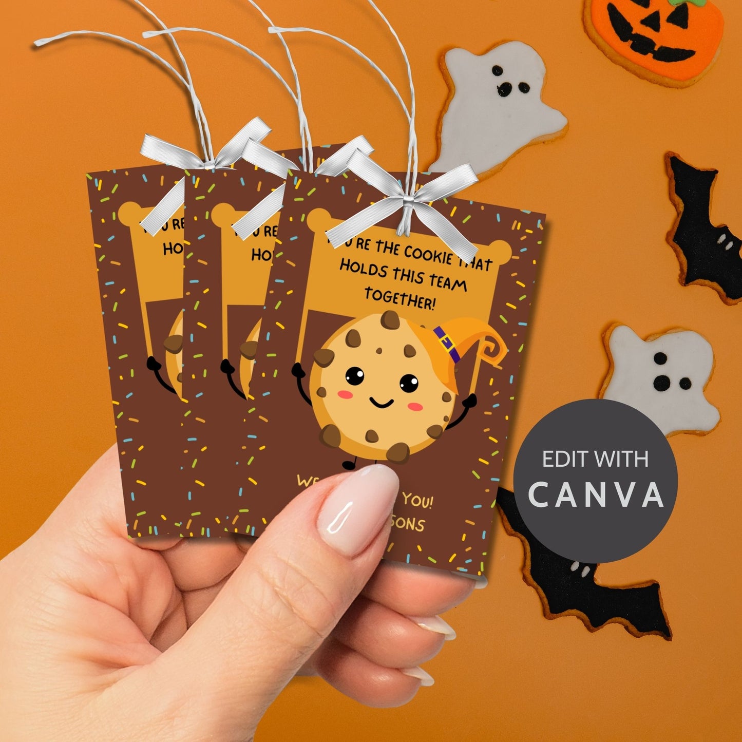 Halloween-themed printable gift tags featuring a cute cookie character in a witch's hat with a sign reading, "You're the cookie that holds this team together!" Tags are 2.5 x 3.5 inches, laid out 8 per sheet on a standard 8.5 x 11-inch page. Includes a printable PDF and a PDF with a link to an editable Canva template.