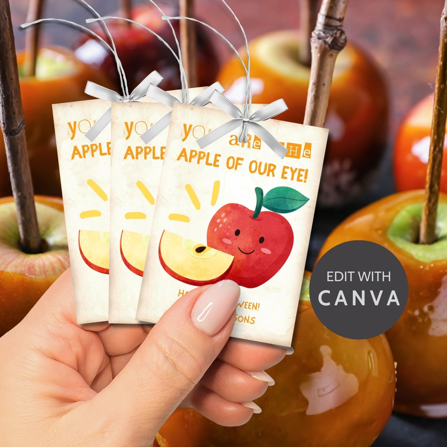 Halloween-themed printable gift tags with the message "You Are the Apple of Our Eye!" featuring a cute apple character perfect for caramel apple gifts. Tags are 2.5 x 3.5 inches, laid out 8 per sheet on a standard 8.5 x 11-inch page. Includes a printable PDF and a PDF with a link to an editable Canva template.