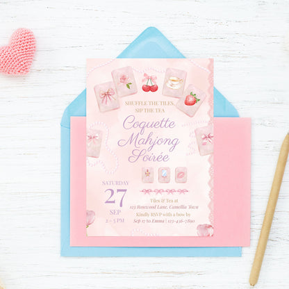 Pink and blue invitation card with game-themed design on a white wooden surface.