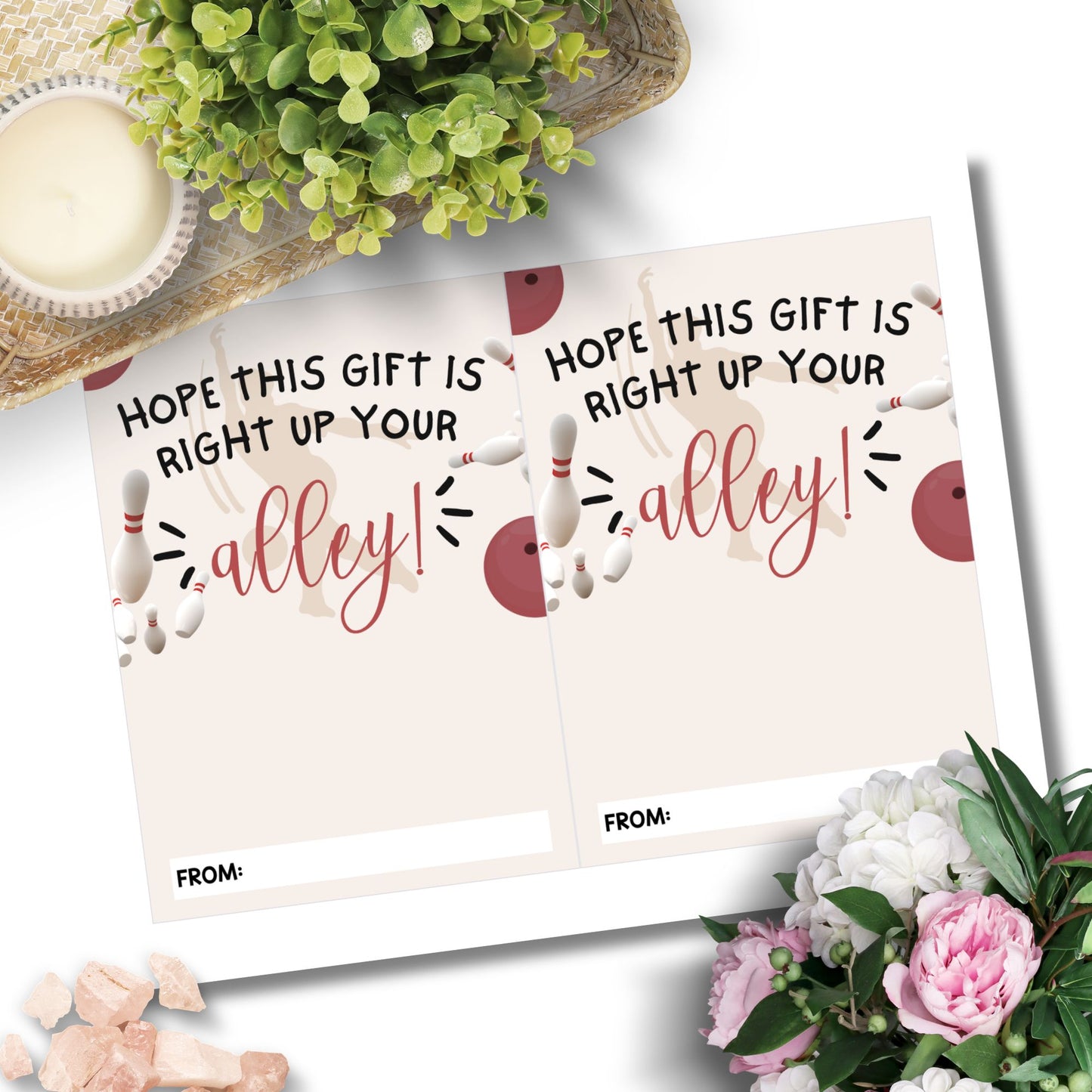 Two personalized bowling-themed gift cards displayed on a white surface with decorative greenery, flowers, and small stones around them. The cards feature bowling pin illustrations and the phrase 'HOPE THIS GIFT IS RIGHT UP YOUR alley!' with a blank 'FROM:' line.
