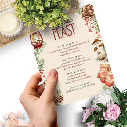 Menu titled 'Cabin Feast' held by a hand with decorative elements like flowers and candles.