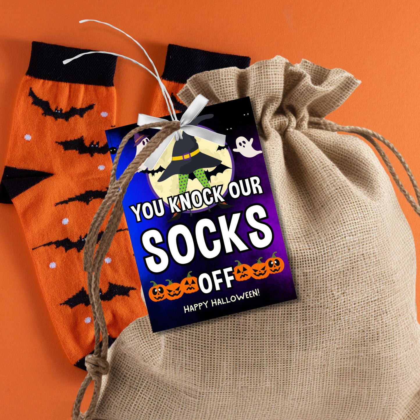 Halloween-themed printable gift tags with the message "You Knock Our Socks Off!" featuring a witch's hat, spooky ghosts, and jack-o'-lanterns, perfect for sock gifts. Tags are 2.5 x 3.5 inches, laid out 8 per sheet on a standard 8.5 x 11-inch page. Includes a printable PDF and a PDF with a link to an editable Canva template.