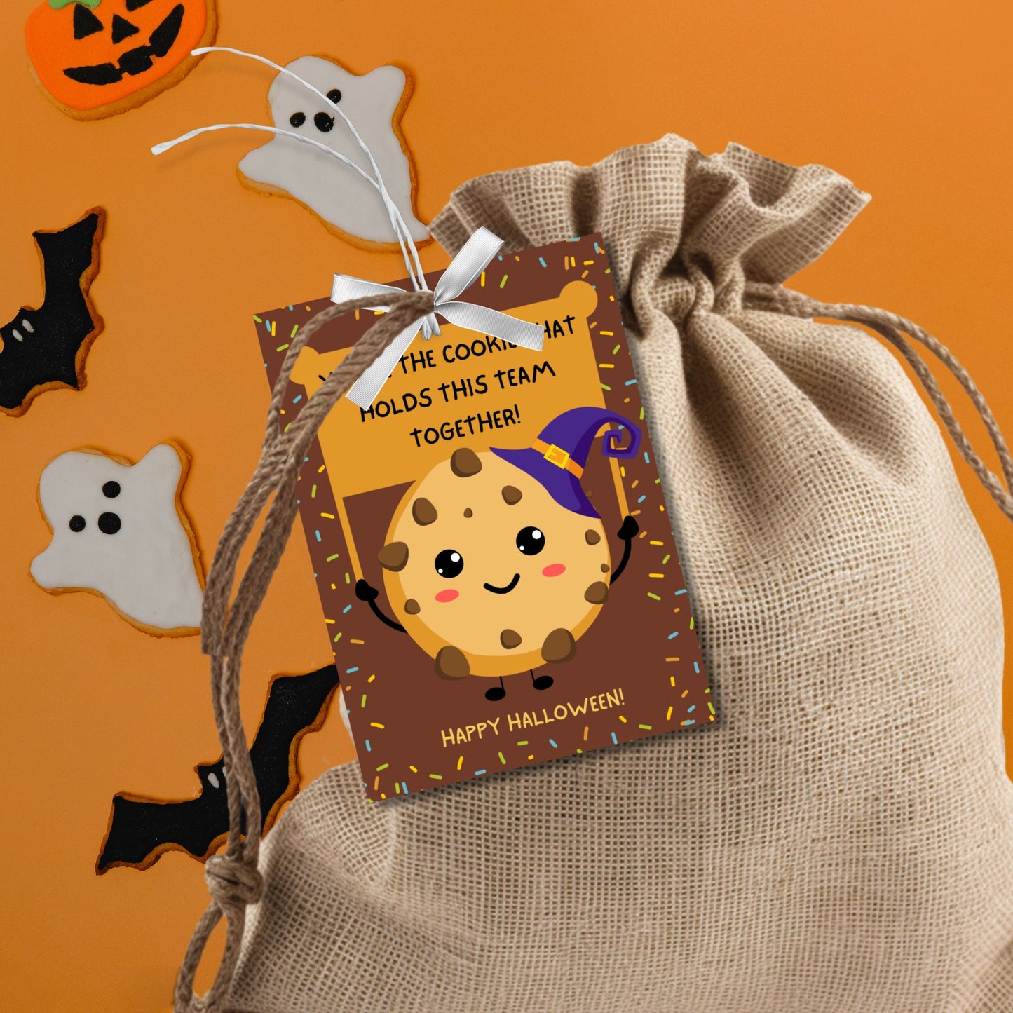 Halloween-themed printable gift tags featuring a cute cookie character in a witch's hat with a sign reading, "You're the cookie that holds this team together!" Tags are 2.5 x 3.5 inches, laid out 8 per sheet on a standard 8.5 x 11-inch page. Includes a printable PDF and a PDF with a link to an editable Canva template.