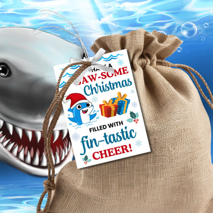 Festive shark-themed holiday gift tags featuring a smiling shark wearing a Santa hat, surrounded by waves, holly, and presents, with the message 'Have a JAW-some Christmas filled with fin-tastic cheer!' Perfect for personalized Christmas gifts.