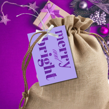 A set of ready-to-print Christmas gift tags featuring bold purple glitter text on a soft lavender background with festive messages like "Merry and Bright" and "Season's Greetings." Each tag measures 2.5 x 3.5 inches, perfect for elegant and vibrant holiday gifting.