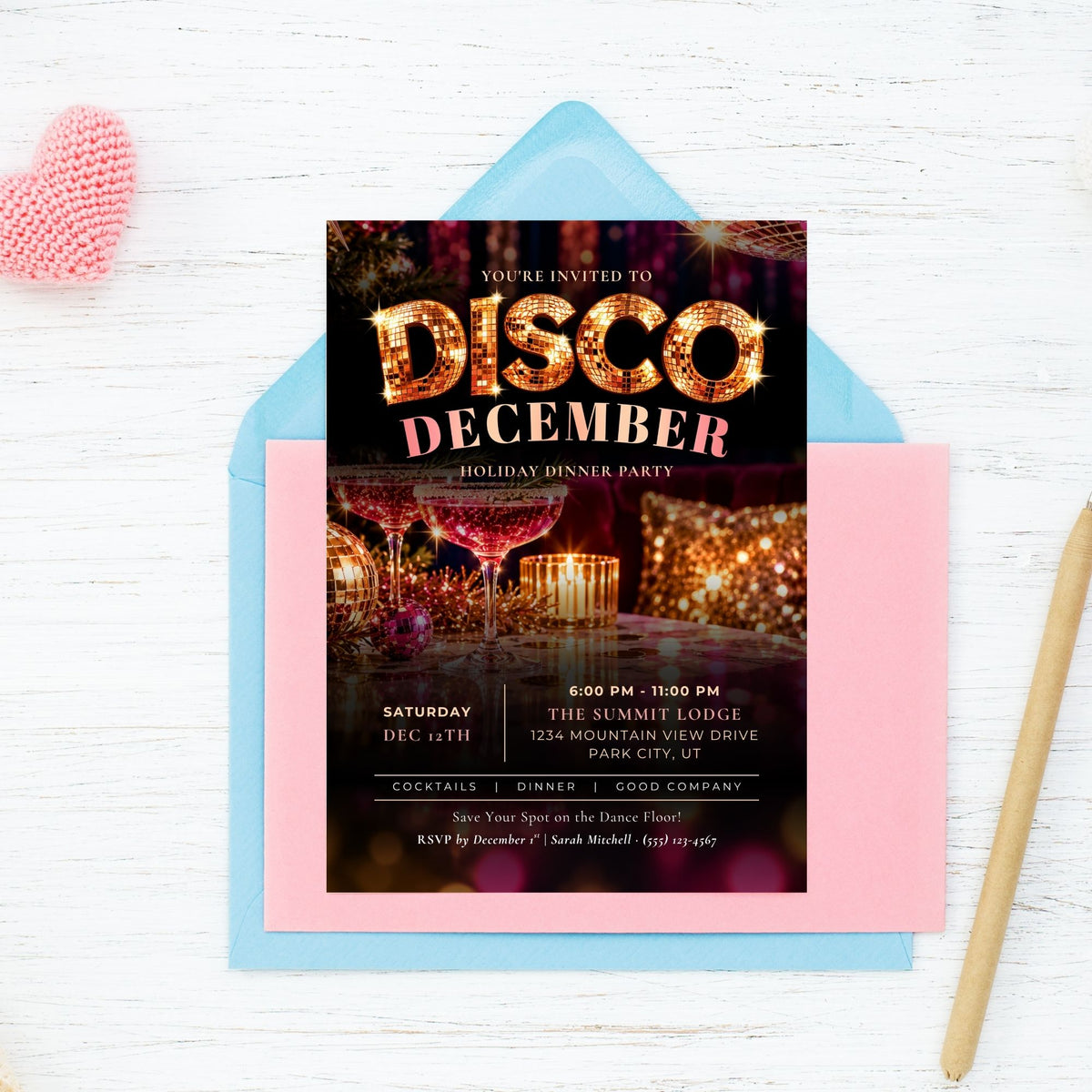 A square party invitation card for a 'Disco December' holiday dinner party, styled in a flat-lay on a light blue envelope and a pink card, set against a white wood background with a pink heart and a wooden spoon.