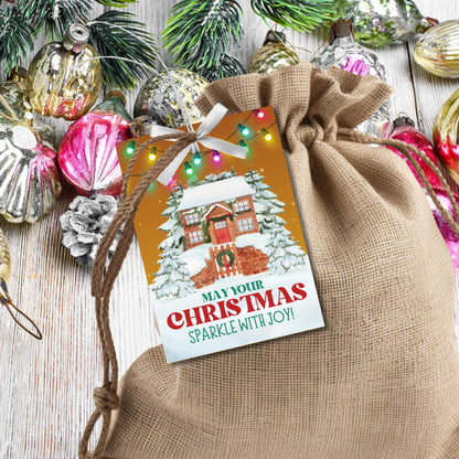 Christmas gift tags featuring a cozy snow-covered house decorated with festive lights, paired with the message "May Your Christmas Sparkle with Joy!" These printable and editable tags add a warm and festive touch to holiday gifts.