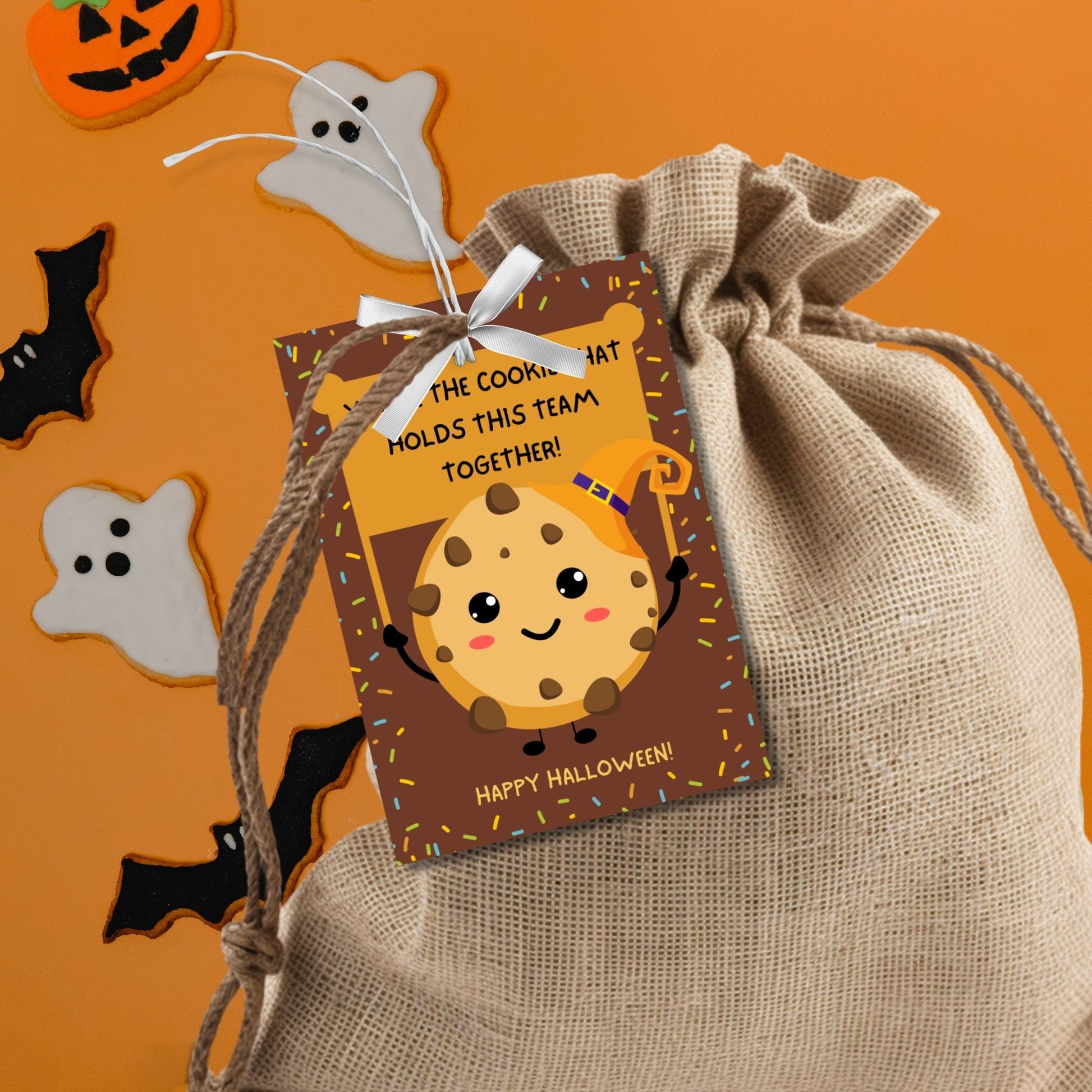 Halloween-themed printable gift tags featuring a cute cookie character in a witch's hat with a sign reading, "You're the cookie that holds this team together!" Tags are 2.5 x 3.5 inches, laid out 8 per sheet on a standard 8.5 x 11-inch page. Includes a printable PDF and a PDF with a link to an editable Canva template.