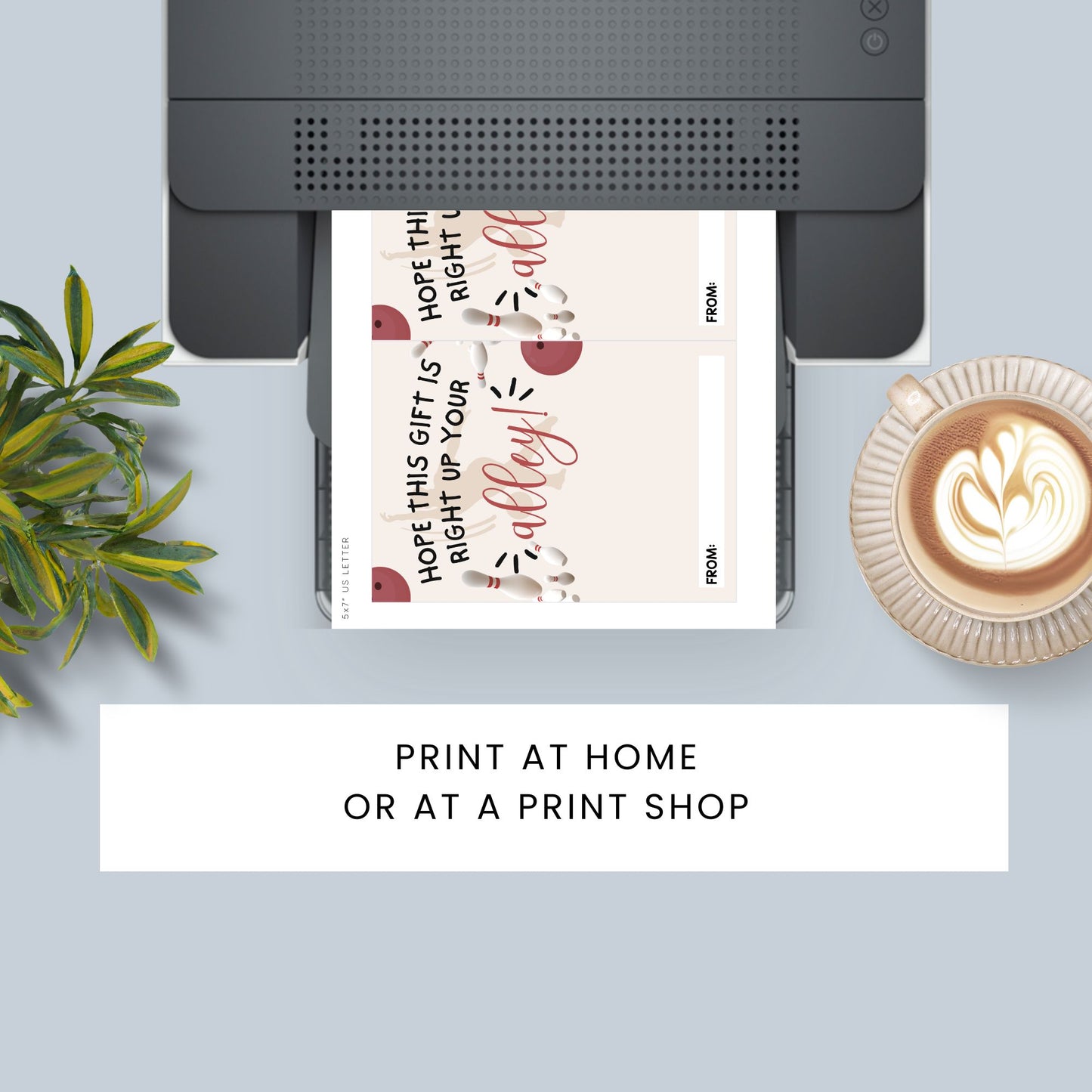 A top-down styled flat lay showing a printer with a printed gift tag sheet emerging, alongside a plant, a cup of latte, and a text banner reading 'PRINT AT HOME OR AT A PRINT SHOP'. The gift tag has a cream background with red and black decorative text and illustrations.