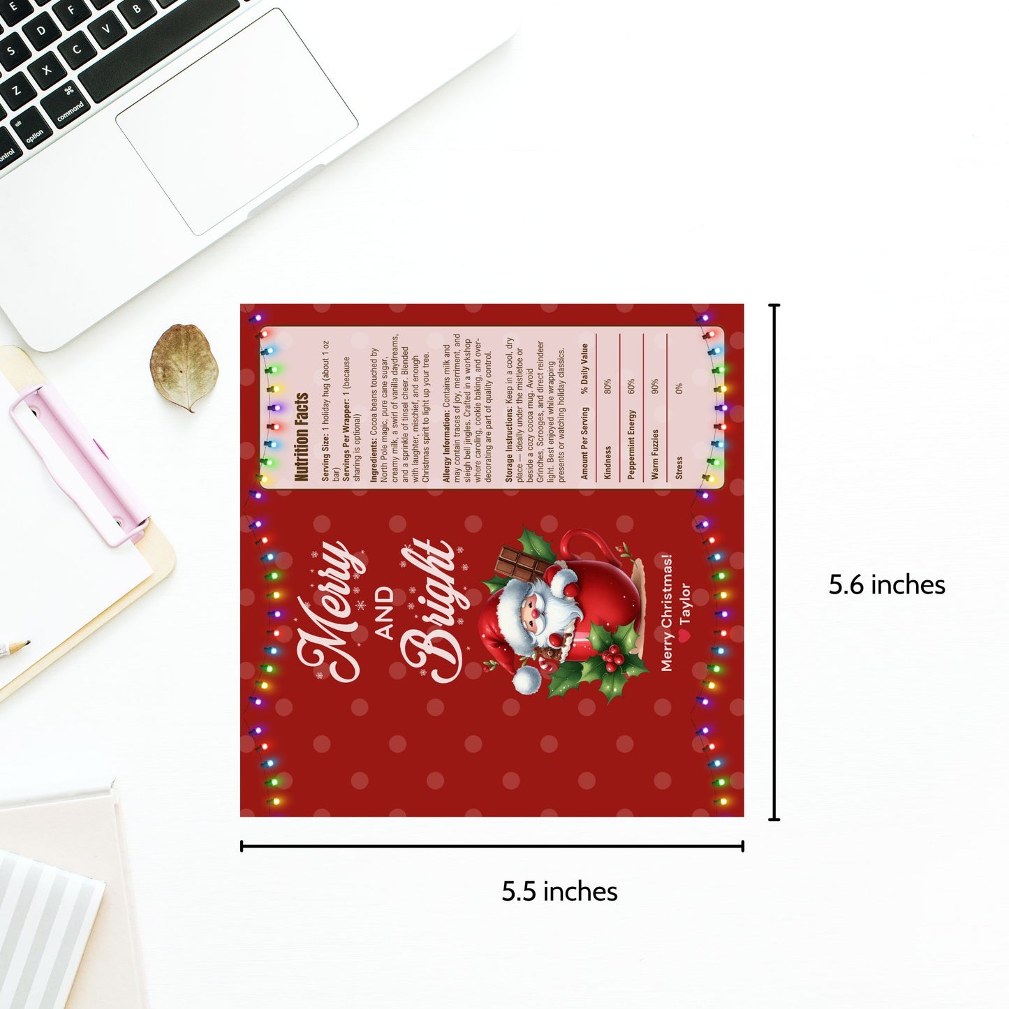 Red Christmas-themed card with Santa Claus design and text, placed on a white surface with a laptop.