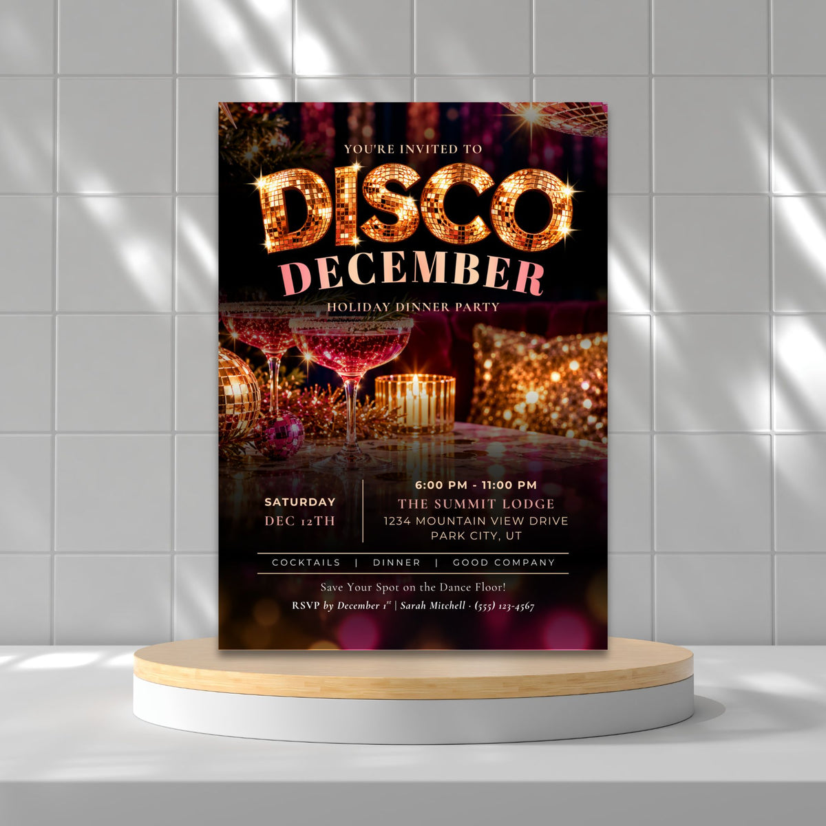A vertical disco December party invitation card displayed upright on a round white and light wood pedestal against a white tiled wall with soft window shadows.