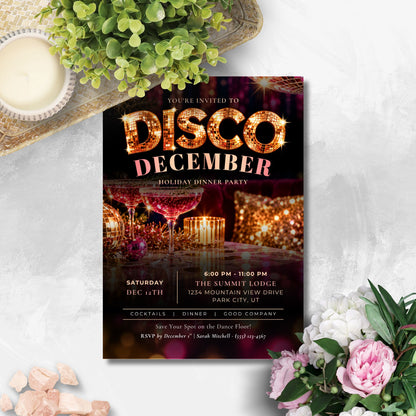 A square party invitation card for a 'Disco December' holiday dinner party, styled in a flat-lay arrangement with a green plant, a lit candle, and pink and white flowers on a light gray textured background.