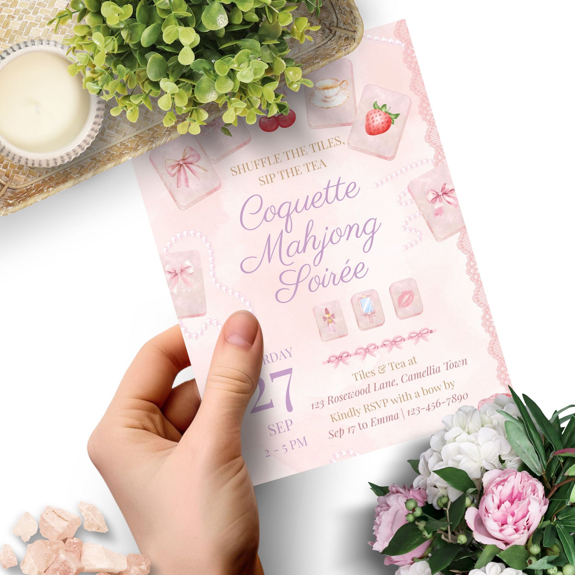 Hand holding a pink Coquette Mahjong Soiree invitation with decorative elements on a white background