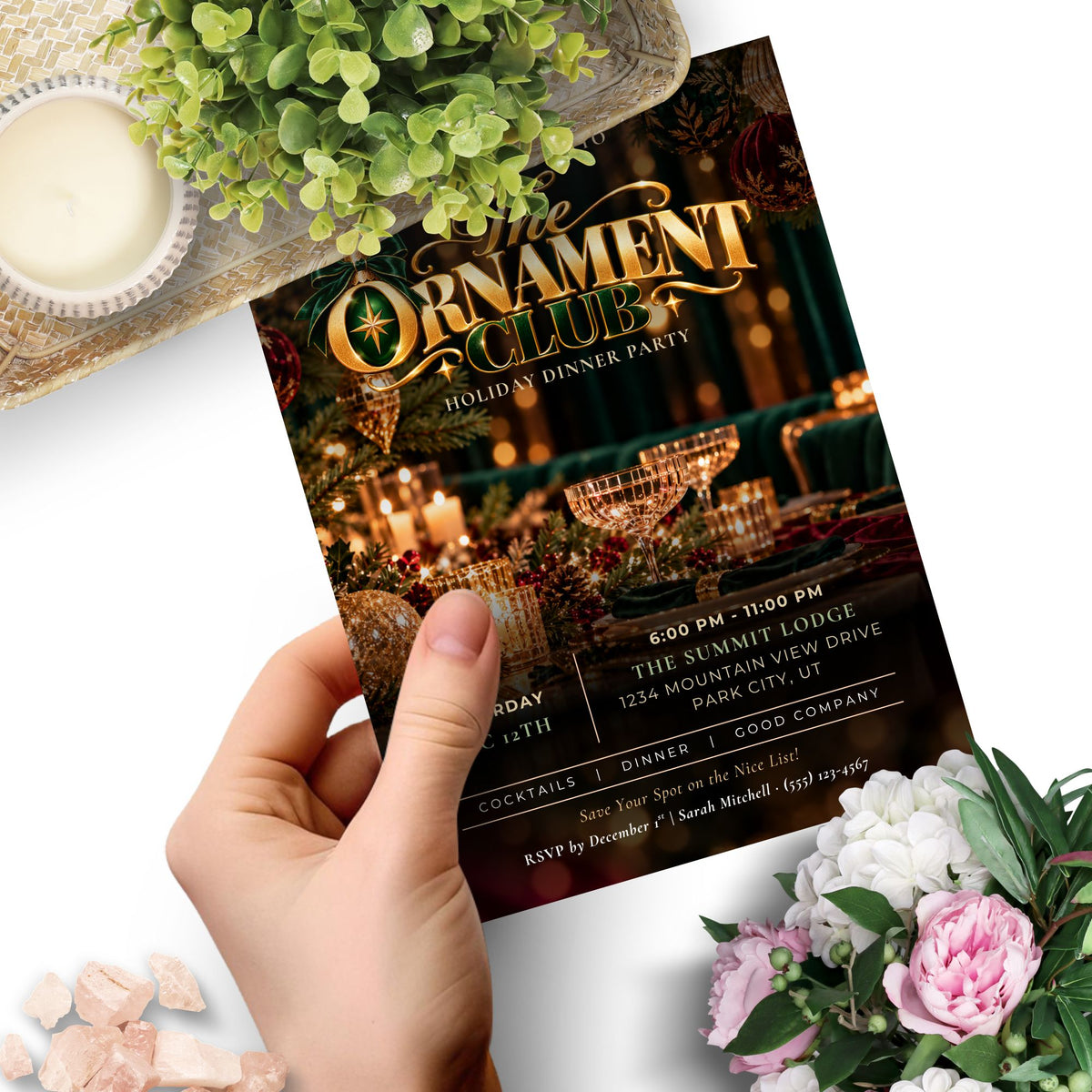 A hand holds a printed invitation card for 'The Ornament Club' holiday dinner party. The card features a dark festive design with gold lettering and a warm holiday table scene.