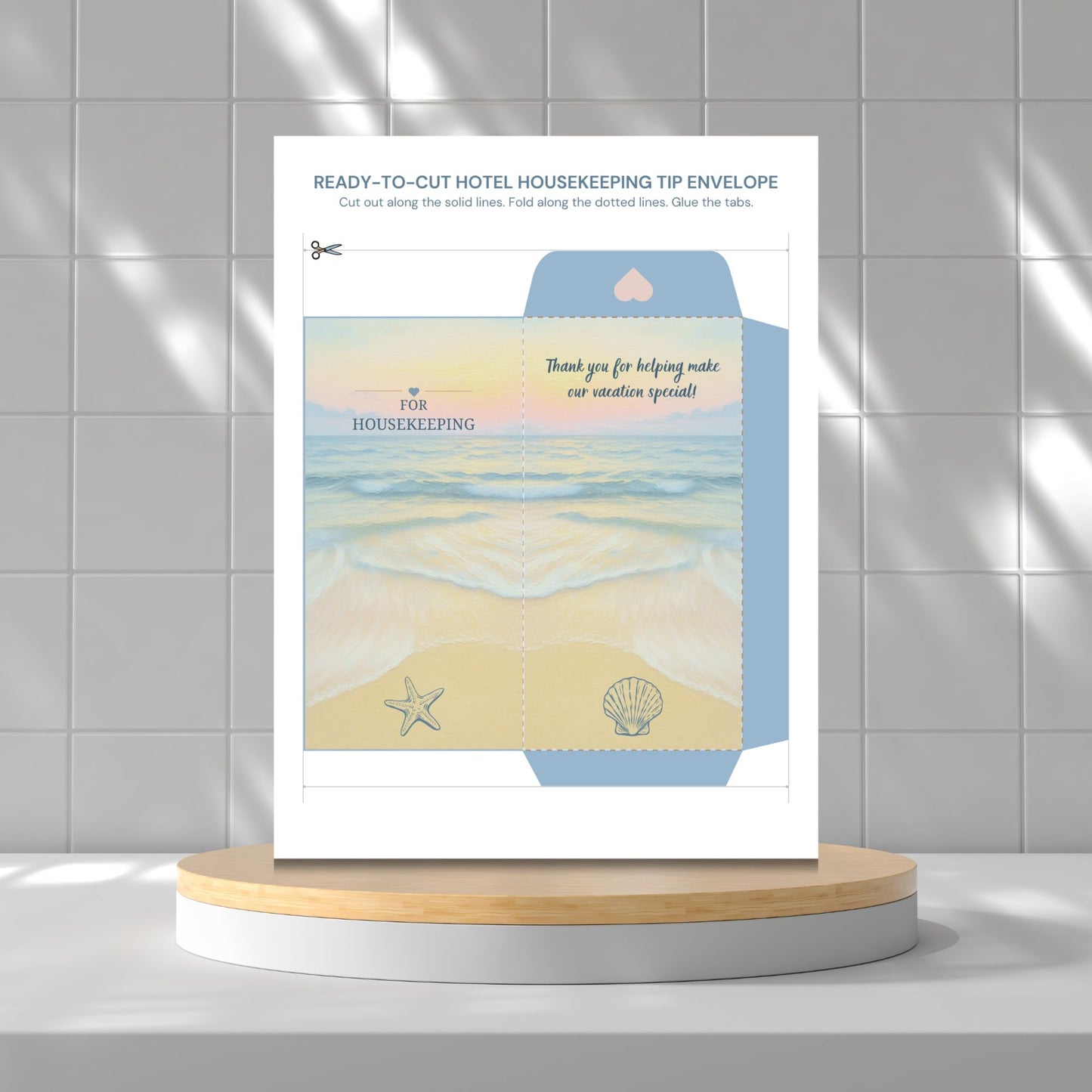 A printed housekeeping tip envelope template or packaging insert displayed upright on a round wooden pedestal against a light gray tiled wall. The insert has beach-themed artwork with blue water, pale yellow sand, a starfish, a shell, and text including 'thank you for helping make our vacation special!' and 'FOR HOUSEKEEPING'.