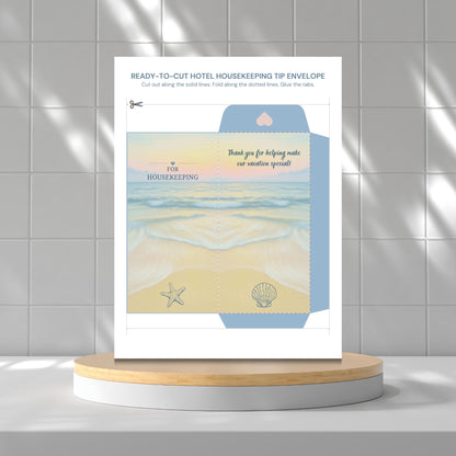 A printed housekeeping tip envelope template or packaging insert displayed upright on a round wooden pedestal against a light gray tiled wall. The insert has beach-themed artwork with blue water, pale yellow sand, a starfish, a shell, and text including 'thank you for helping make our vacation special!' and 'FOR HOUSEKEEPING'.