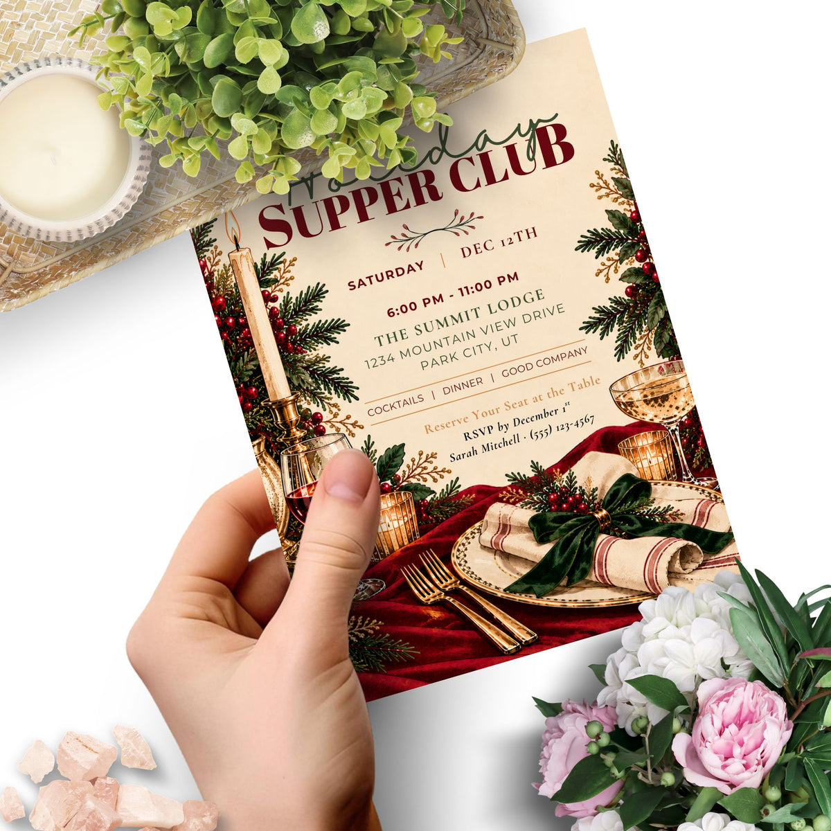 A hand holds a printed invitation card for a 'Holiday Supper Club' with a festive Christmas table setting design. The card features red and gold typography, pine branches, and holiday decorations.