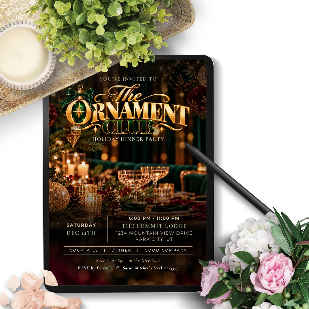 A digital invitation template displayed on a tablet screen, styled with a pen, green leaves, pink flowers, and crystals on a white background. The invitation features a festive holiday theme with gold lettering and warm candlelit imagery.